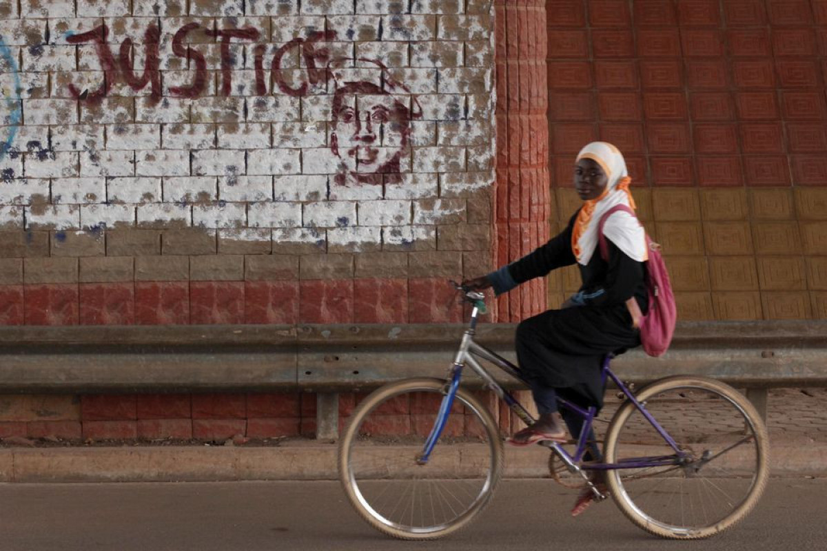 A girl rides a bicycle past graffiti reading "Justice" with a picture of slain ex-President Thomas Sankara in Ouagadougou, Burkina Faso